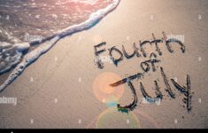 Fourth Of July Message Written For The American Independence Day Holiday In Smooth Sand With Sunny Lens Flare View Of An Incoming Wave On The Beach Image259373633
